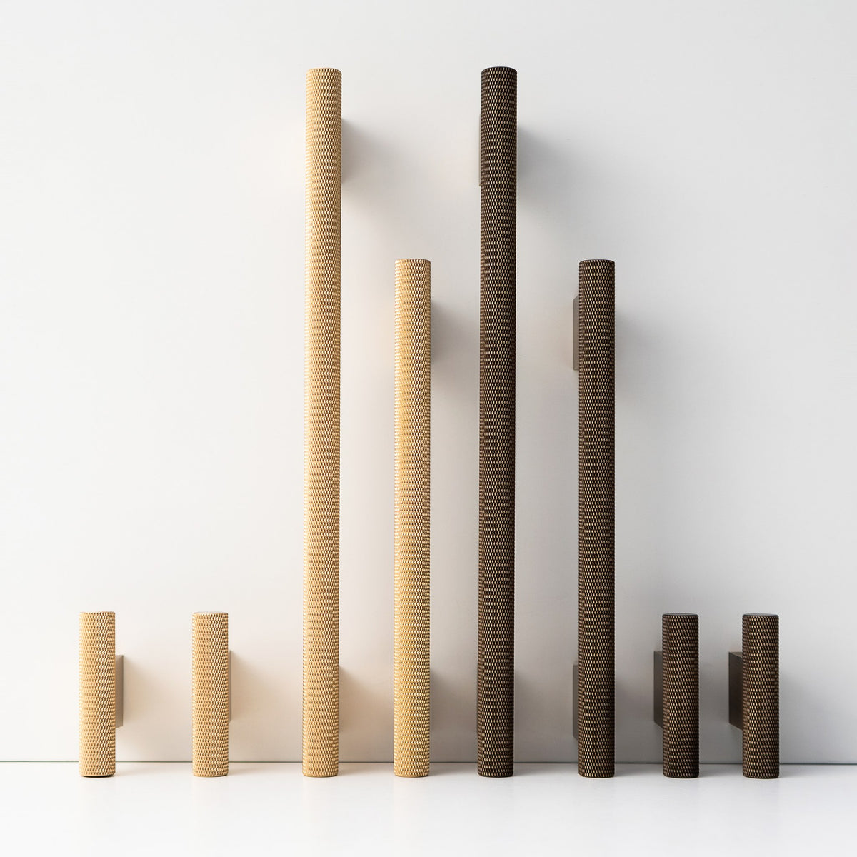 HELIOS knurled brass handles and T-pulls standing in a row, Satin Brass and Antique Brass